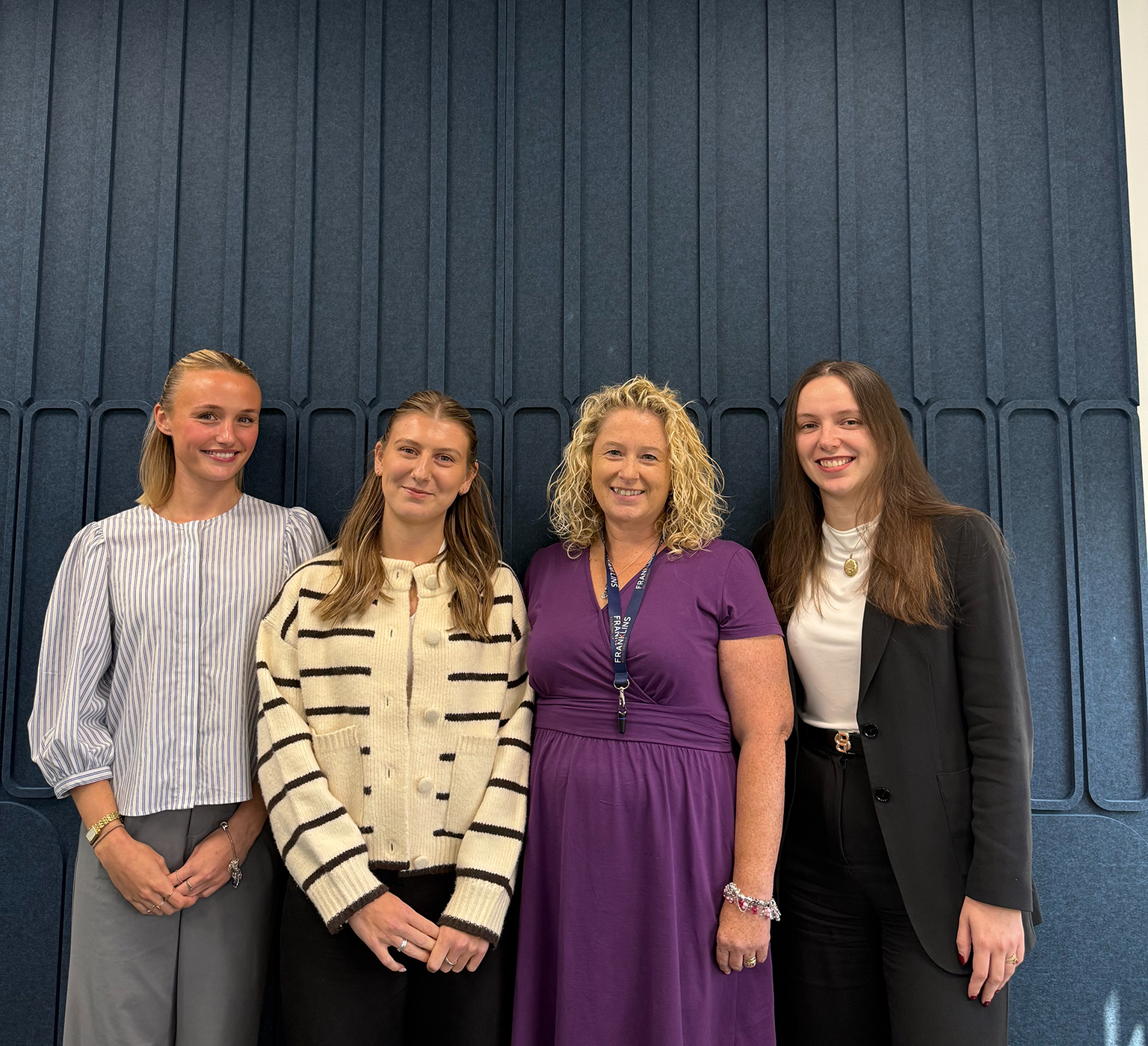 Four members of the Franklins Solicitors team standing together and smiling in front of a navy panelled wall at the firm's office.