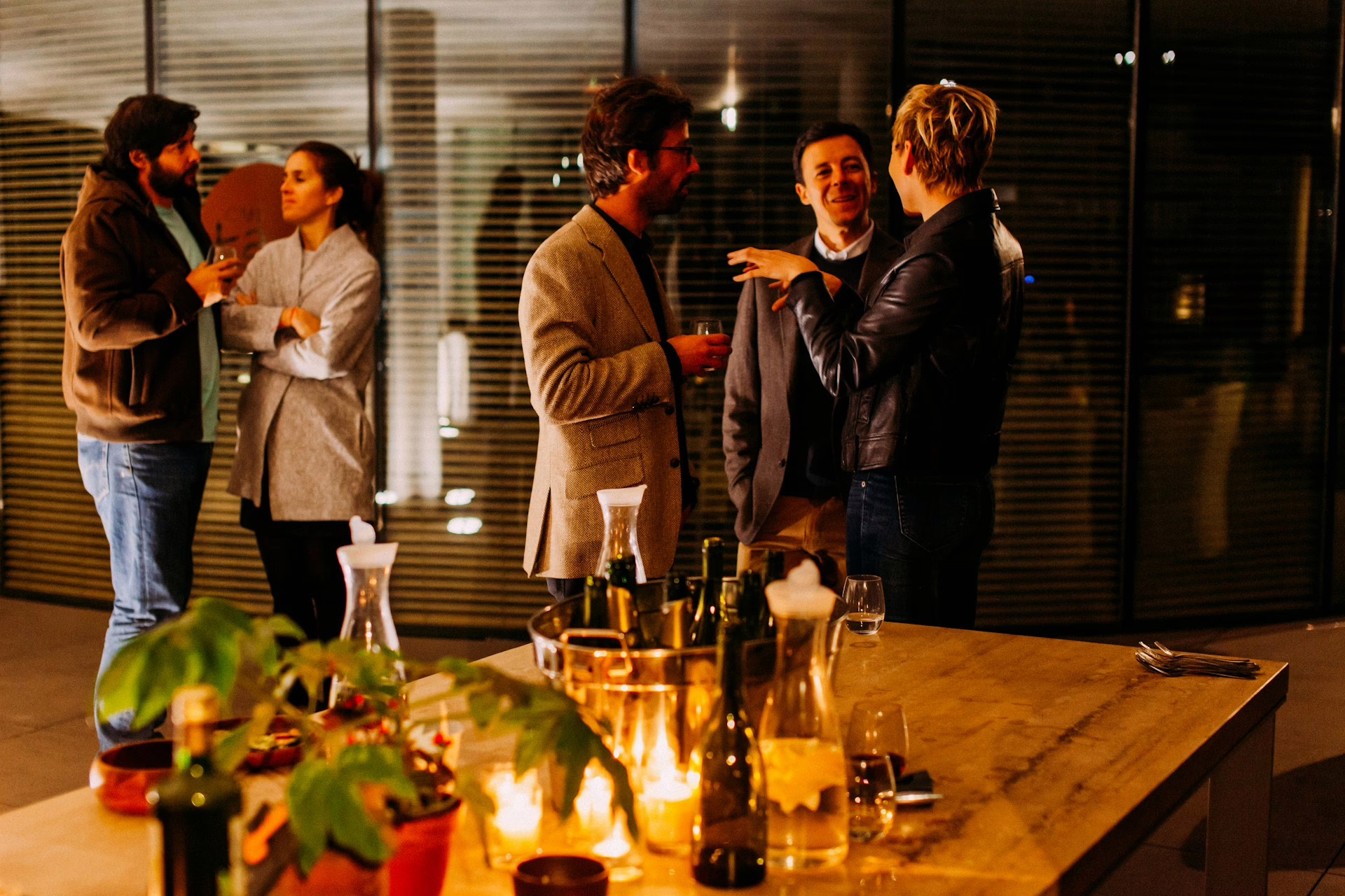 Office colleagues socialising and talking around a table with drinks at a workplace event.