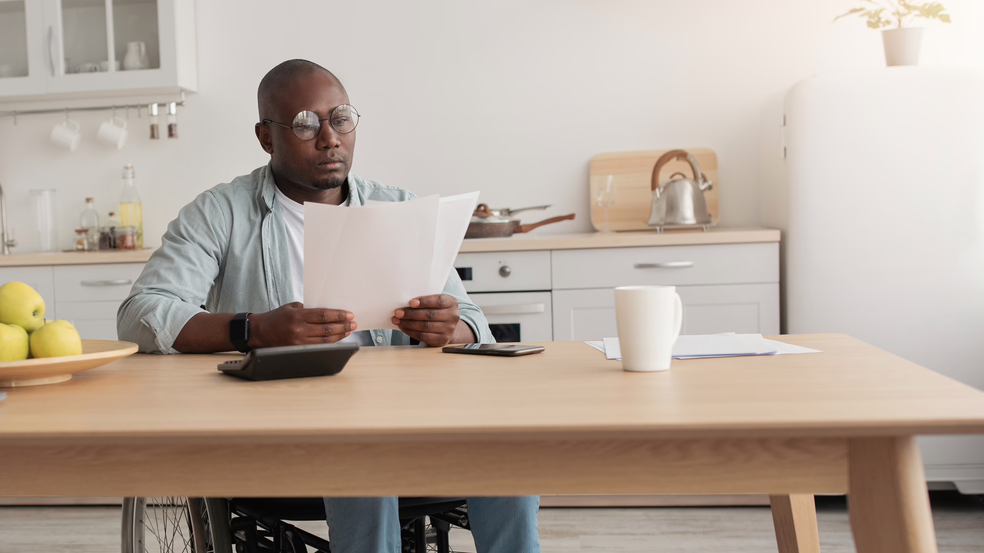 Person sitting at a kitchen table reviewing official documents with a serious expression.