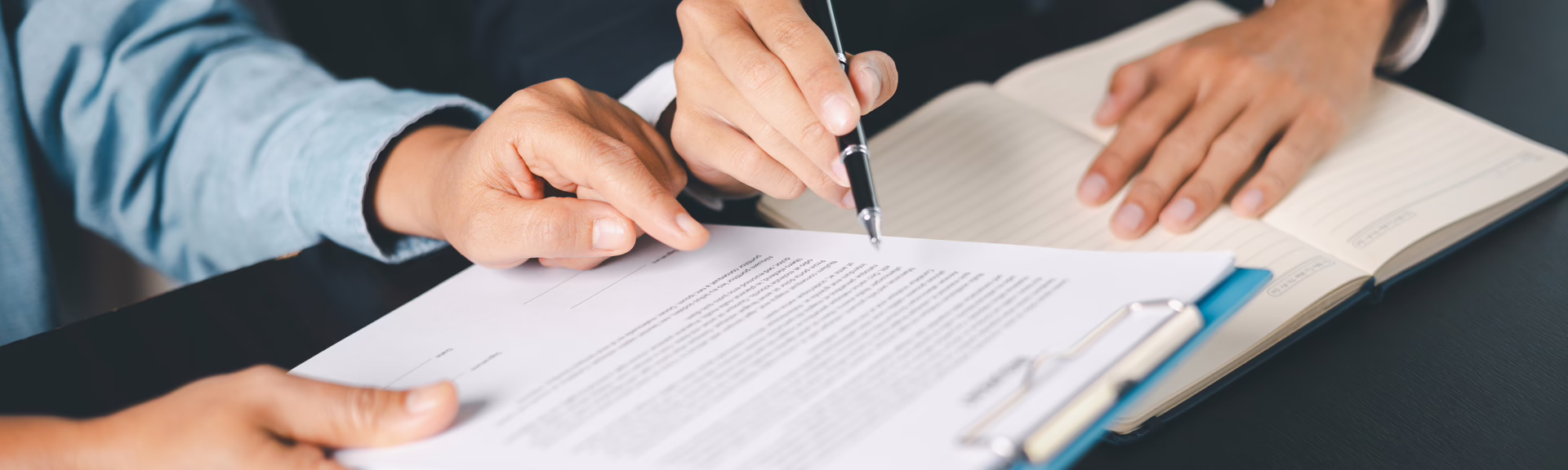Close-up of two individuals reviewing and discussing a formal legal agreement at a desk.