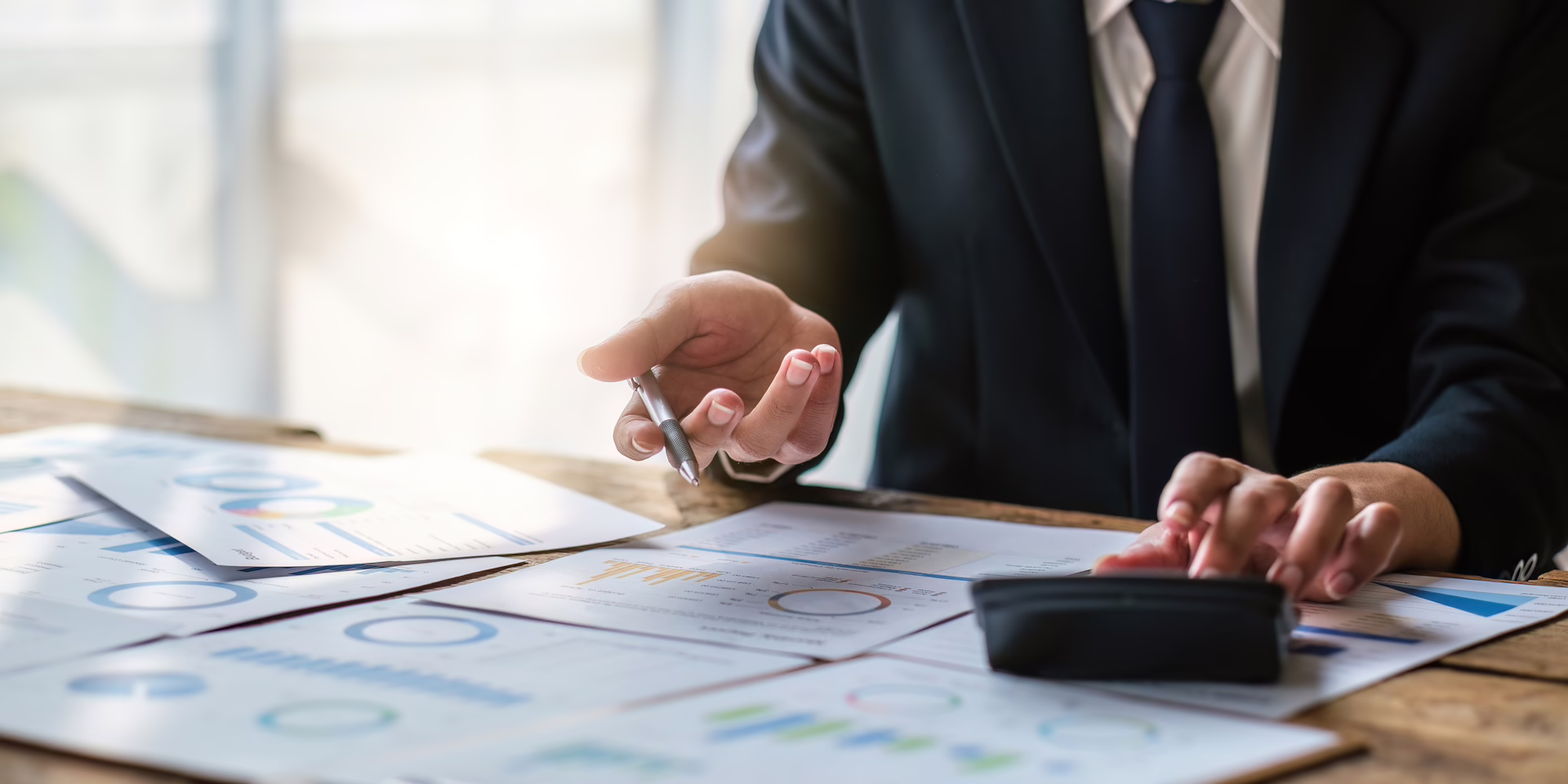 Professional reviewing financial charts and calculations at a desk with documents and a calculator.