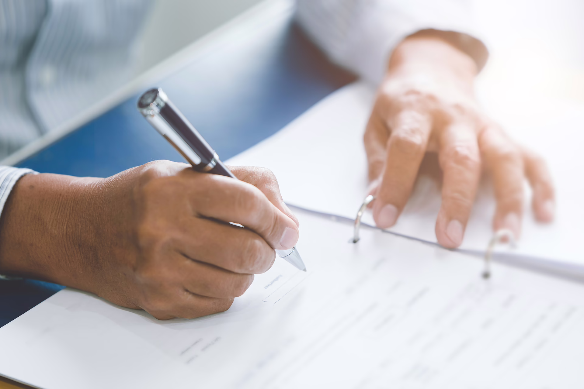 Person signing documents in a folder with a pen at a desk in a professional setting.