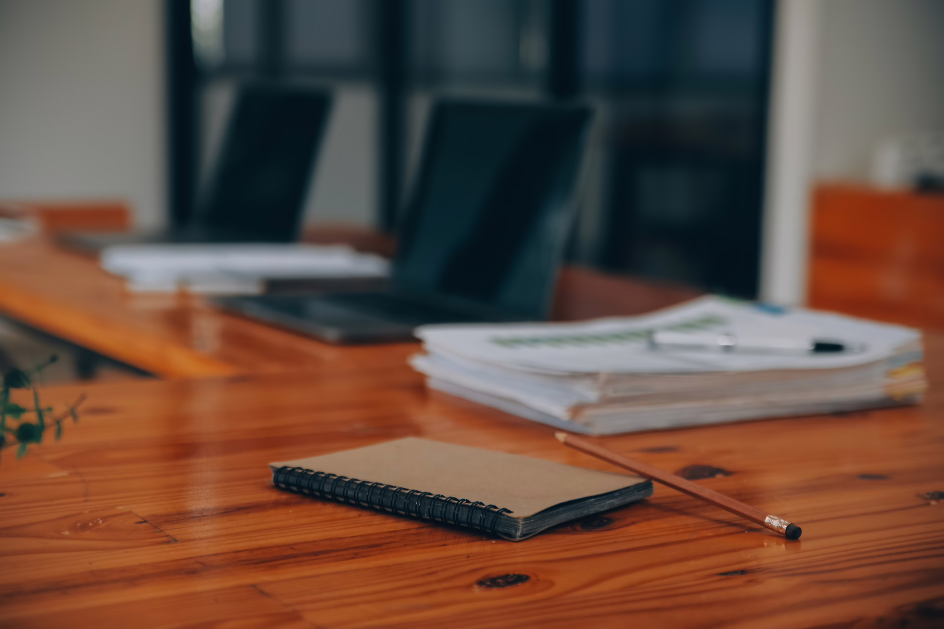 Notebook, pencil and stacks of documents laid out on a meeting table in a professional office setting.