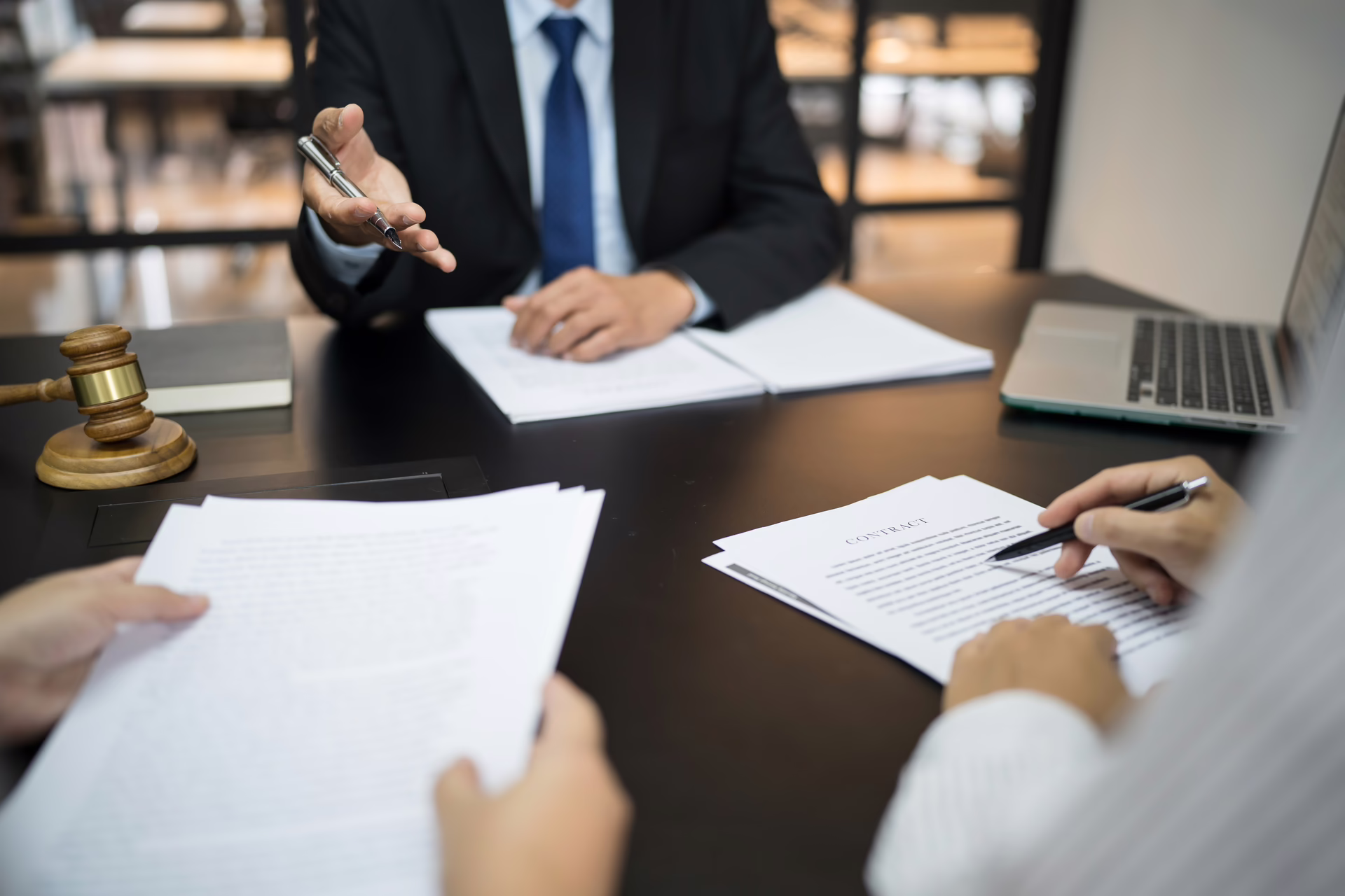 Business professionals reviewing and signing legal documents at a meeting table with a gavel visible nearby.