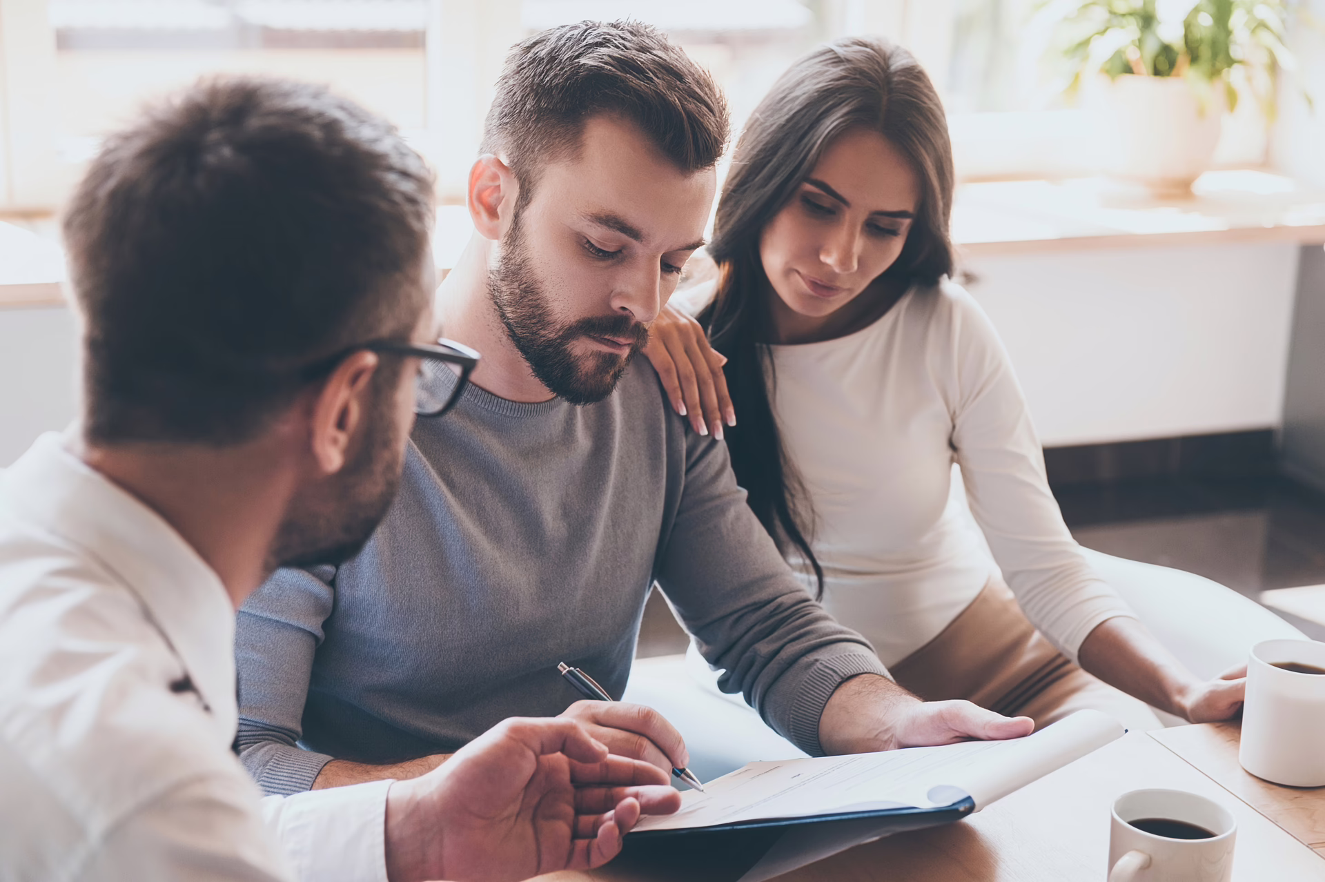 Three people seated together reviewing a document at a table in a bright room.