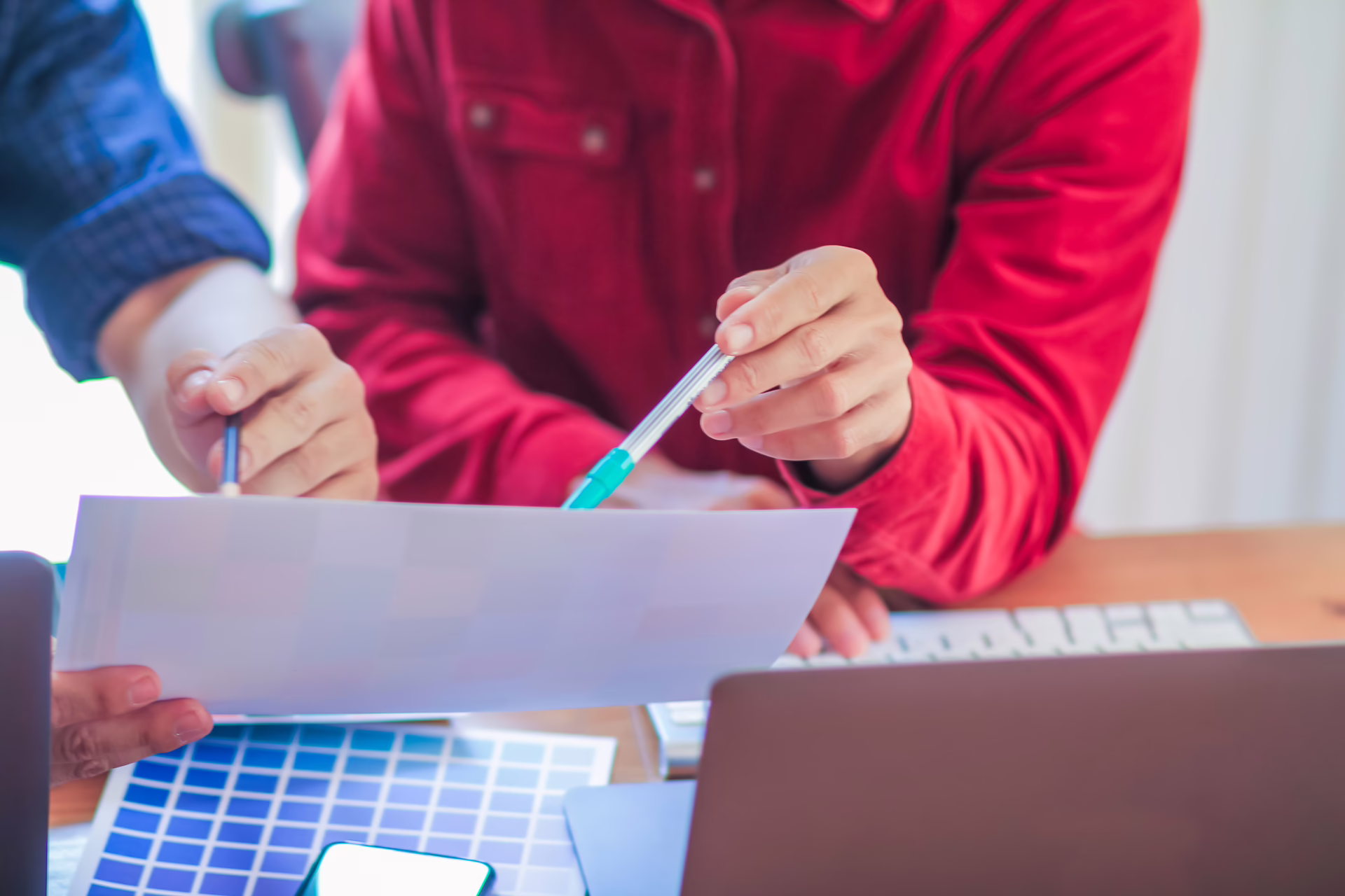 Two professionals reviewing printed materials and colour samples at a desk with a laptop nearby.