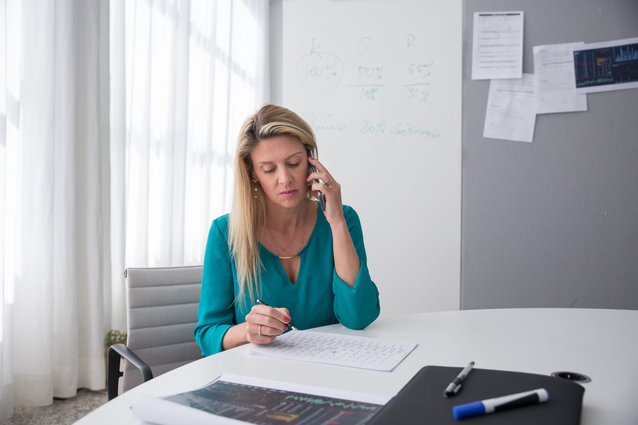 A woman making notes on a document while talking on the phone in an office