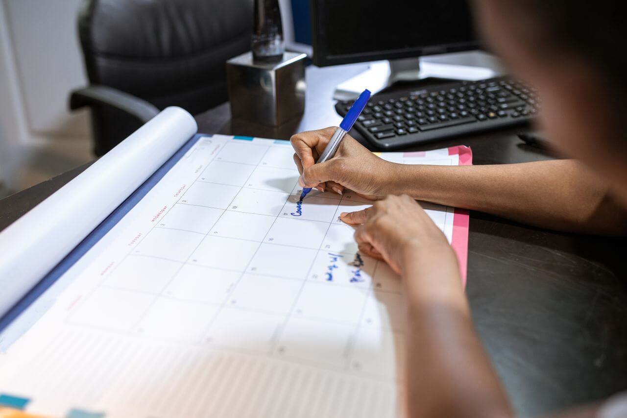 Person marking dates in a desk planner at an office desk