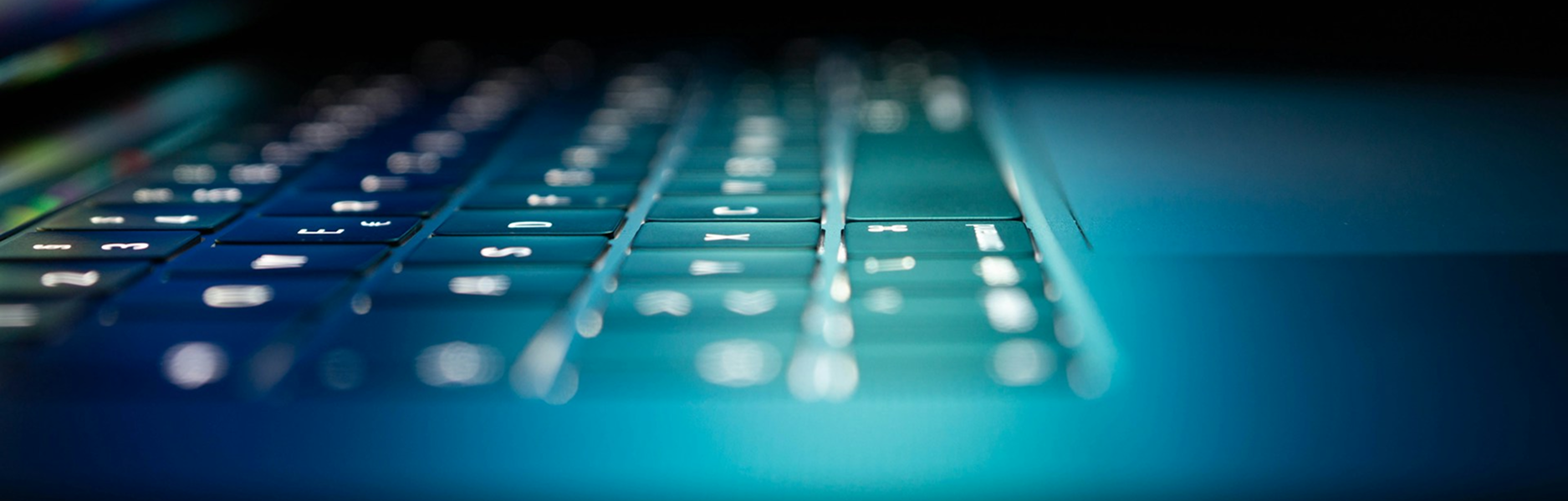 Close-up of an open laptop keyboard lit by blue screen light in a dark room